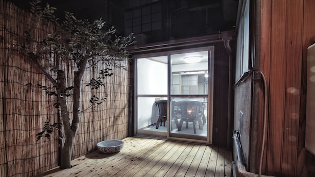 Una habitación con piso de madera, pared de bambú y puerta corredera de vidrio que da a otra habitación.