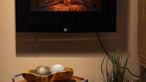 Ein Flachbildfernseher an der Wand über einem Holztisch mit Dekoration und einer Topfpflanze.