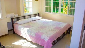A bedroom with a bed, a window with a view of greenery, and a shelf with towels. - Cottages at Hill Resort (Pak Chong)