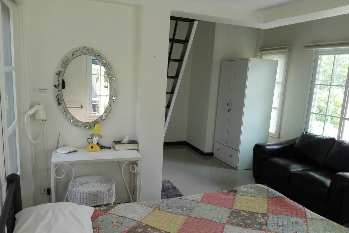 Un dormitorio con cama, escritorio con lámpara, espejo, armario y ventana.