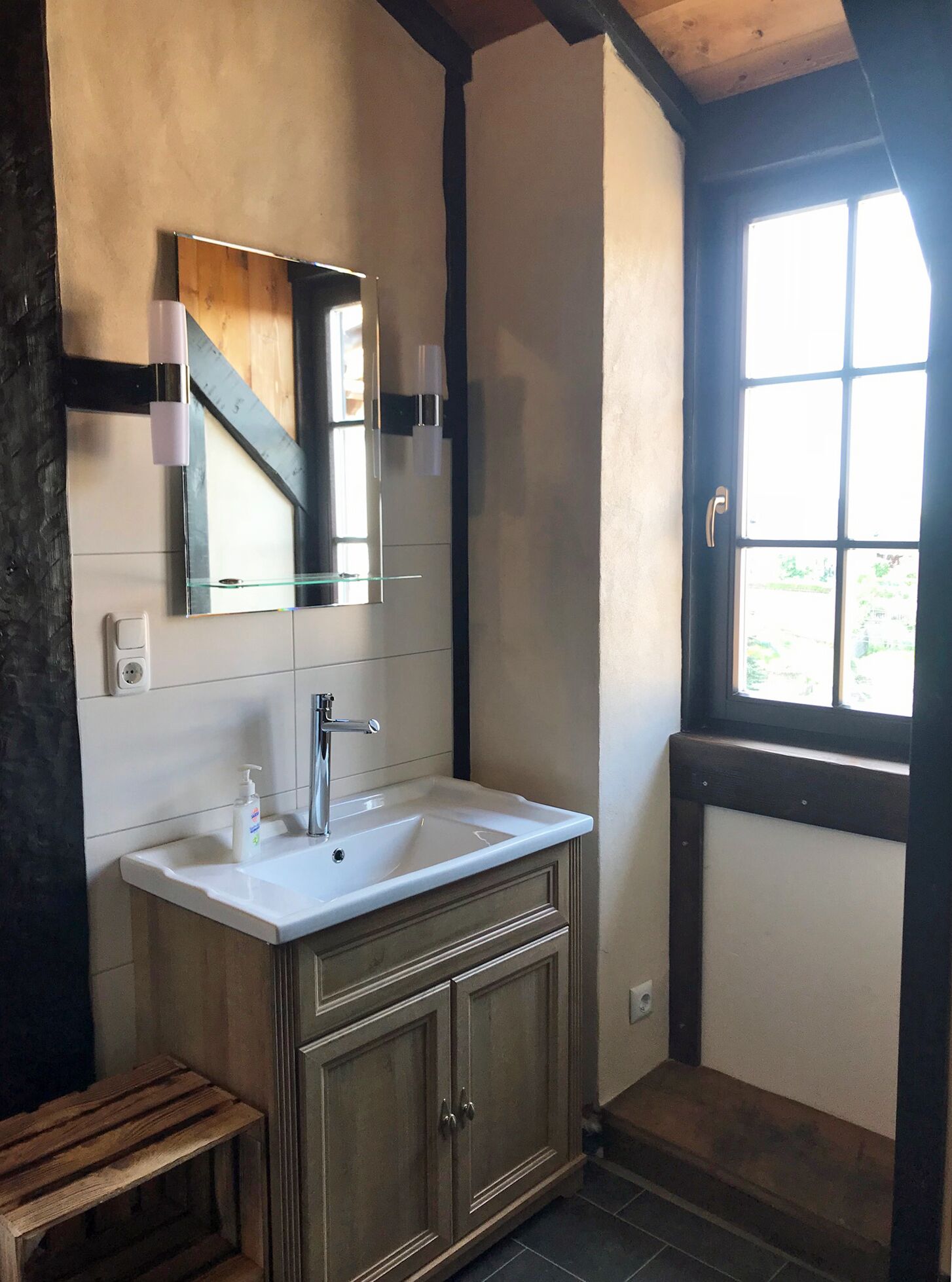 A bathroom with a white sink, wooden cabinets, a mirror, and a window.