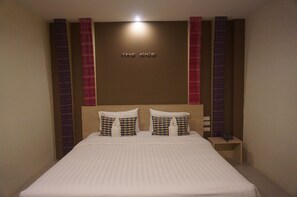 A neatly made bed with checkered pillows, a wooden headboard, and a wall with vertical stripes and a sign reading "THE RICE".