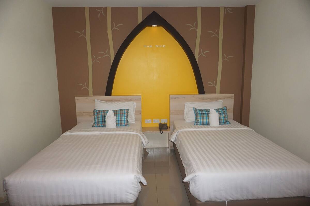 A hotel room with two beds, a wall-mounted telephone, and a decorative arch with the text "THE RICE".