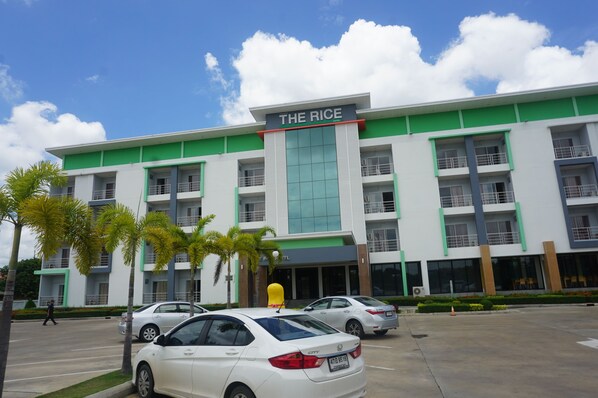 A multi-story hotel named "The Rice" with a green and white exterior, multiple balconies, and a parking lot with cars.