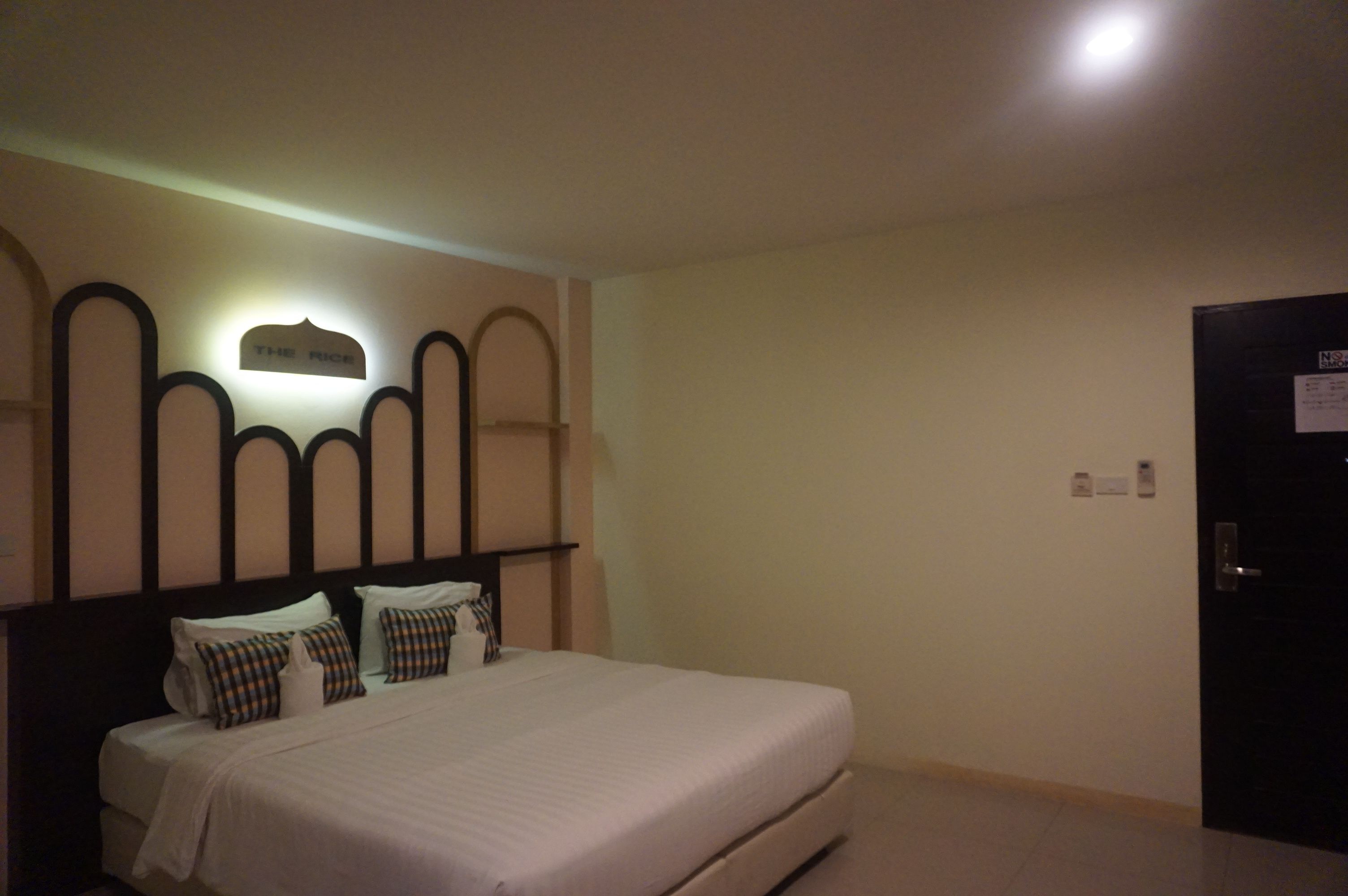 A hotel room with a bed, a headboard with a sign, and a door.