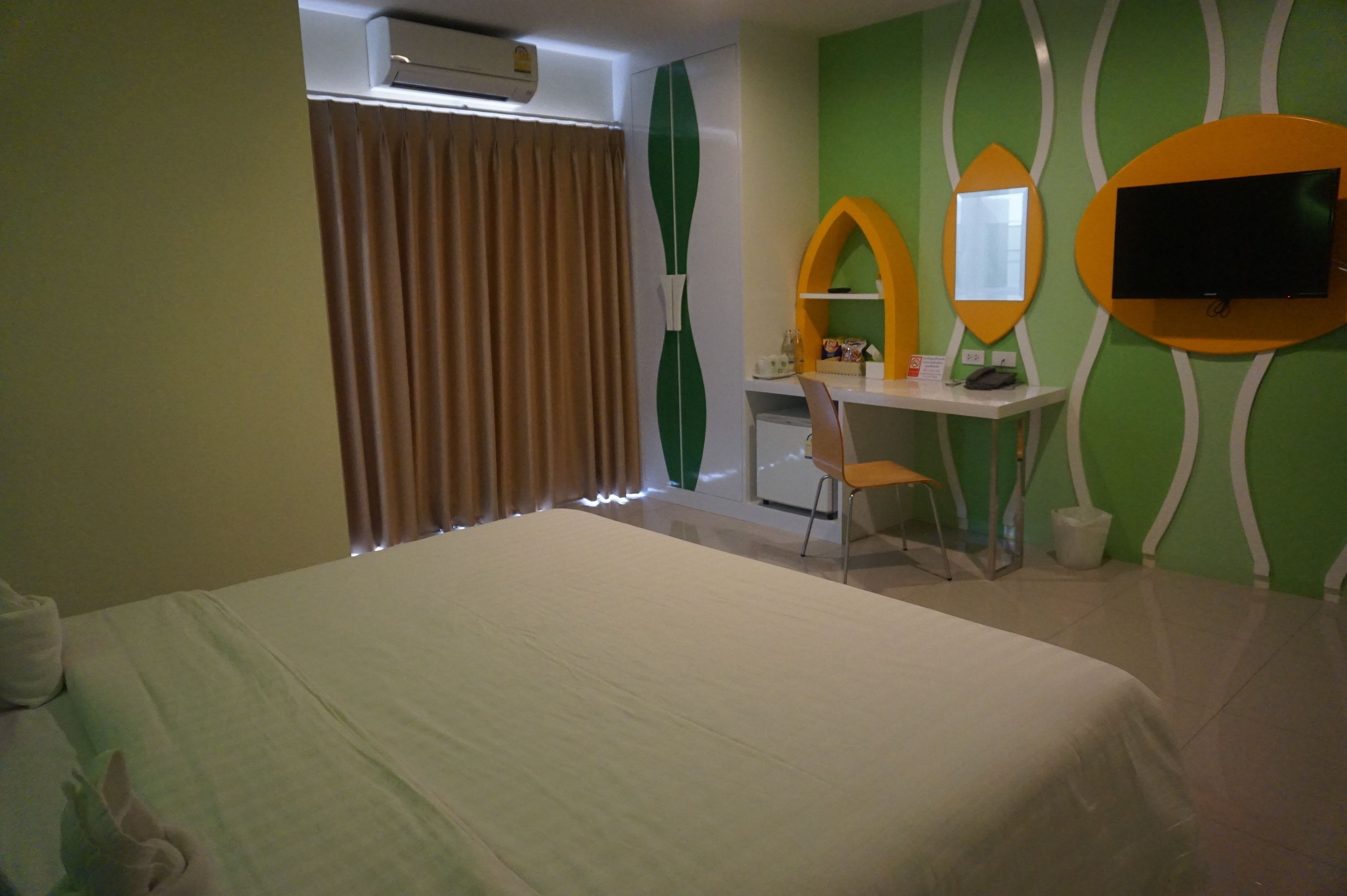 A hotel room with a bed, a desk with a chair, a television, and a window with curtains.