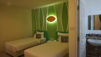 A hotel room with two single beds, a green accent wall, a wall-mounted light, and a bathroom with a sink and mirror.