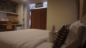Una habitación de hotel con cama, almohadas, una silla, un escritorio y una cortina.