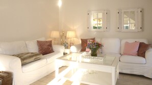 Ein Wohnzimmer mit zwei weißen Sofas, einem Glastisch und einem Beistelltisch mit Lampen.