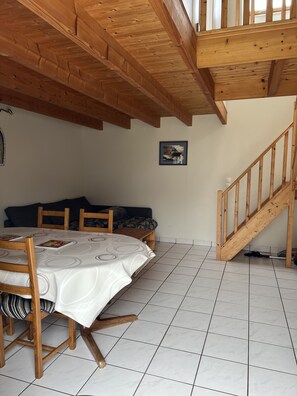Un espace repas comprenant une table et des chaises en bois, un canapé et un escalier.