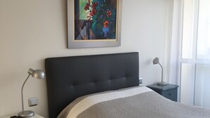 Una camera da letto con un letto grande, un comodino con una lampada, un quadro appeso al muro e una finestra con tende.