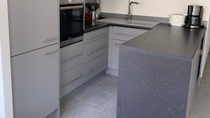 Una cucina moderna con mobili grigi, forno a incasso, microonde, macchina del caffè e lavello.