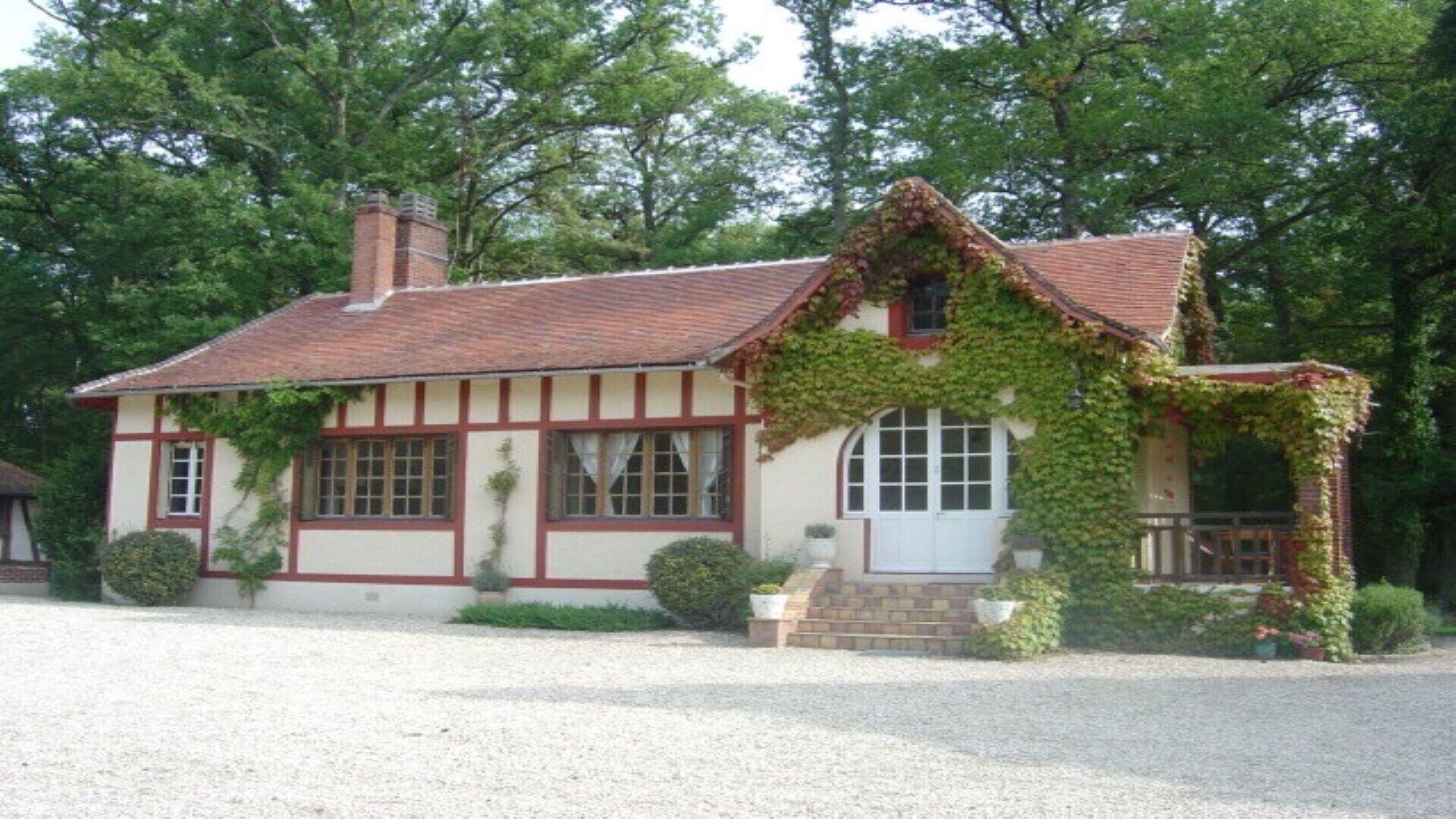A traditional half-timbered house with a red-tiled roof, ivy-covered walls, and a gravel driveway.