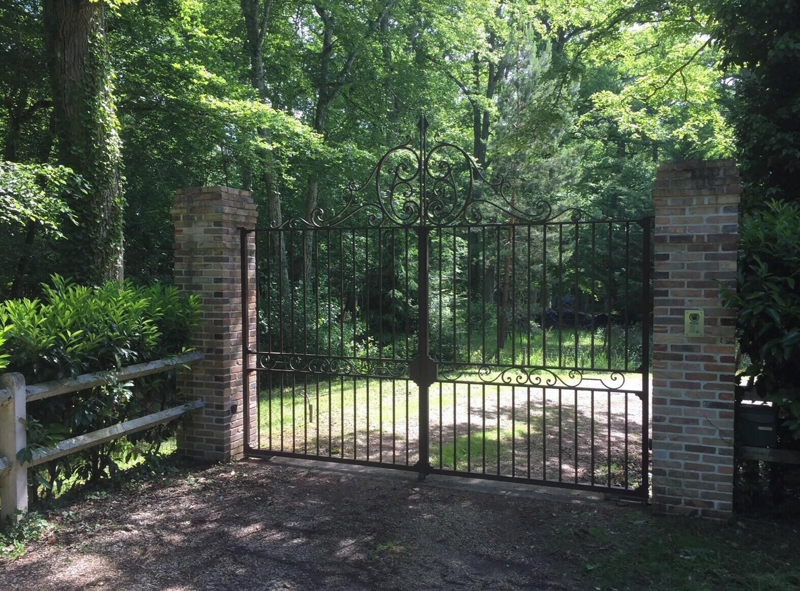 A gated entrance with a brick wall and metal gate, surrounded by lush greenery.