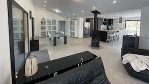 A modern kitchen with a central island, a dining area with a glass table, and a living space with a black sofa and a coffee table. - Superb farmhouse in a beautiful green setting, breathtaking view of the Canigou  (Vivès)
