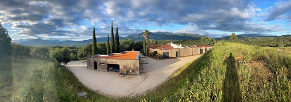 A modern building with a red roof, surrounded by lush greenery and mountains in the background. - Superb farmhouse in a beautiful green setting, breathtaking view of the Canigou (Vivès)