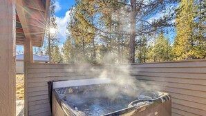 Ett bubbelbad på ett trädäck med utsikt över träd och en byggnad i bakgrunden.