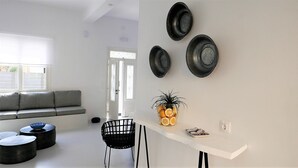 A modern living room with a grey sofa, black chairs, and a white table with decorative plates and a plant. - 30villa Rd in Rhodes (Rodos)