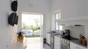 A modern kitchen with white cabinets, a stainless steel range hood, and a window overlooking a garden. - 30villa Rd in Rhodes (Rodos)