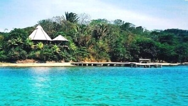 Ein Resort mit zwei Häusern mit Reetdach, einem Steg und einem Strand.