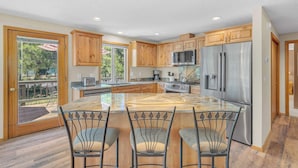 A modern kitchen with wooden cabinets, stainless steel appliances, and a large island with bar stools. - AC, foosball, near play ground, hot tub (Sunriver)