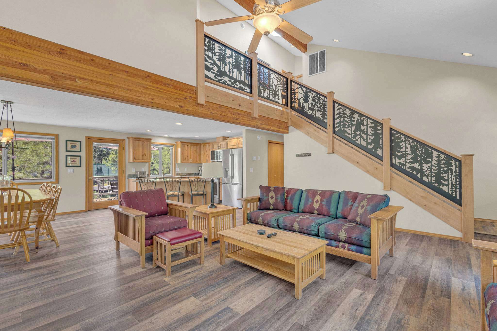 A spacious living area with a wooden staircase, a sofa, a coffee table, and a dining set.