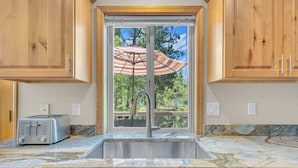 A kitchen with wooden cabinets, a marble countertop, a stainless steel sink, and a window with an umbrella. - AC, foosball, near play ground, hot tub (Sunriver)