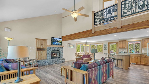 A spacious living room with a fireplace, wooden furniture, and a kitchen area with wooden cabinets and large windows. - AC, foosball, near play ground, hot tub (Sunriver)
