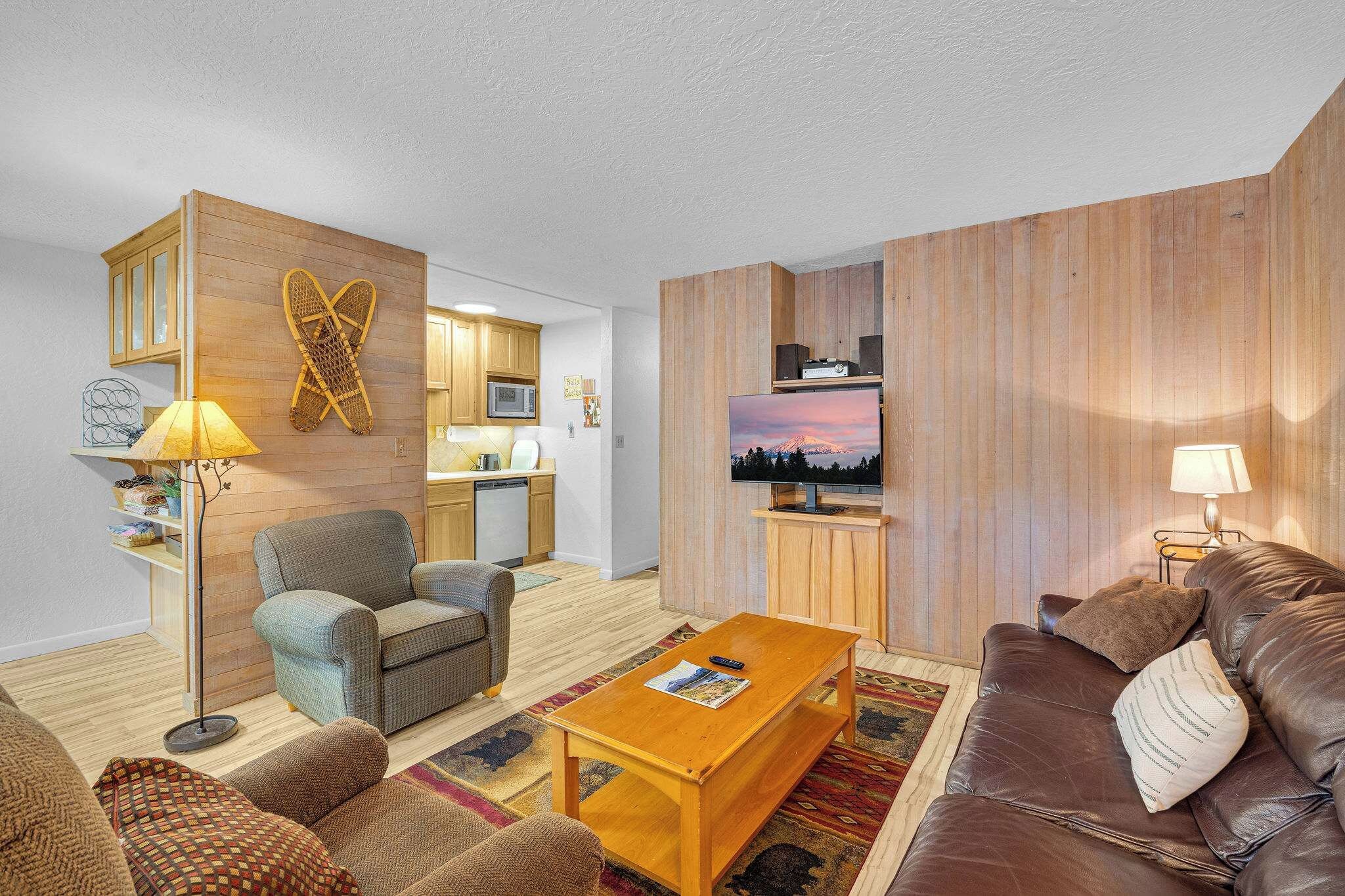 A modern living room with a sofa, armchair, coffee table, and a television mounted on a wooden wall.
