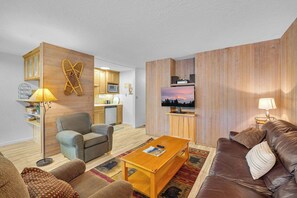 A modern living room with a sofa, armchair, coffee table, and a television mounted on a wooden wall. - Inside Sunriver Village near local shops, eateries (Sunriver)