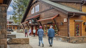 A wooden building with a stone facade, a sign indicating a business, and a paved area in front. - Inside Sunriver Village near local shops, eateries (Sunriver)