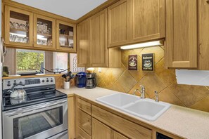 A kitchen with wooden cabinets, a stove, a coffee maker, and a sink. - Inside Sunriver Village near local shops, eateries (Sunriver)