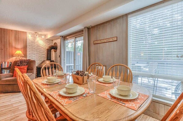 A dining area with a wooden table set for four, surrounded by wooden chairs. A sign on the wall reads "Friends & Family Gather Here." - Inside Sunriver Village near local shops, eateries (Sunriver)