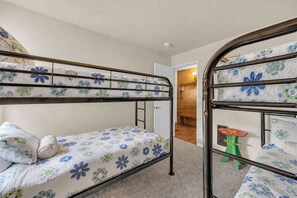 A bunk bed room with floral bedding, a green stool, and a wooden door leading to another room. - Inside Sunriver Village near local shops, eateries (Sunriver)
