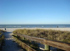 A beach path leading to the ocean with a wooden fence and grass in the foreground.