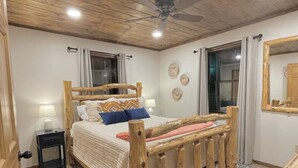 Uma cama de madeira com cabeceira, uma mesinha de cabeceira com abajur e um tapete estampado.