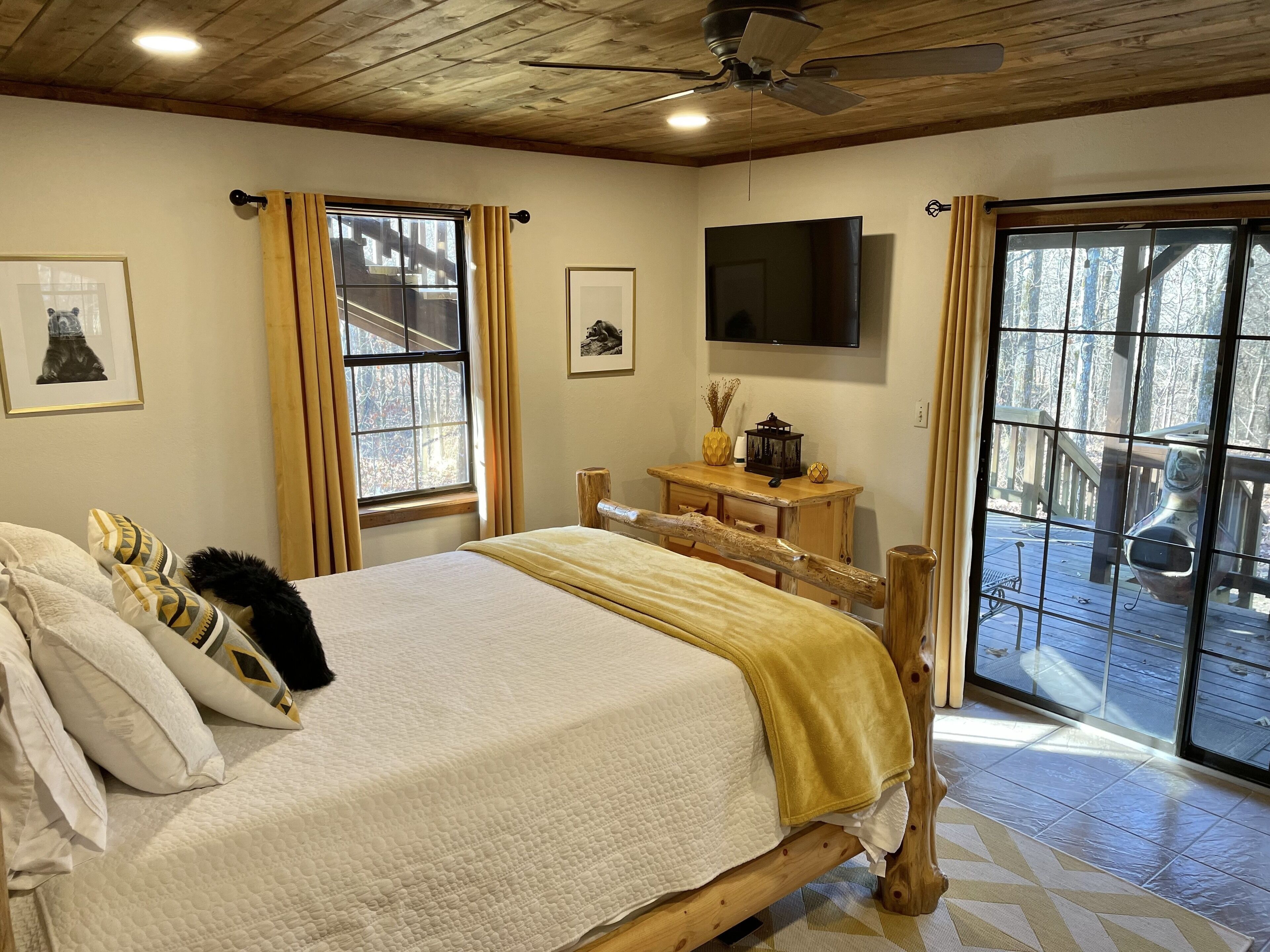 Un dormitorio con cama y mesita de noche de madera, televisión y ventana con cortinas.