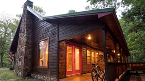 Uma cabana rústica com varanda, base de pedra e uma bicicleta estacionada na frente.