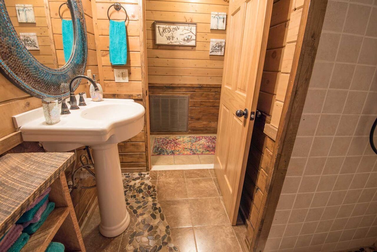 Un baño pequeño con un lavamanos pedestal blanco, paredes de madera, un espejo grande y una ventana pequeña.