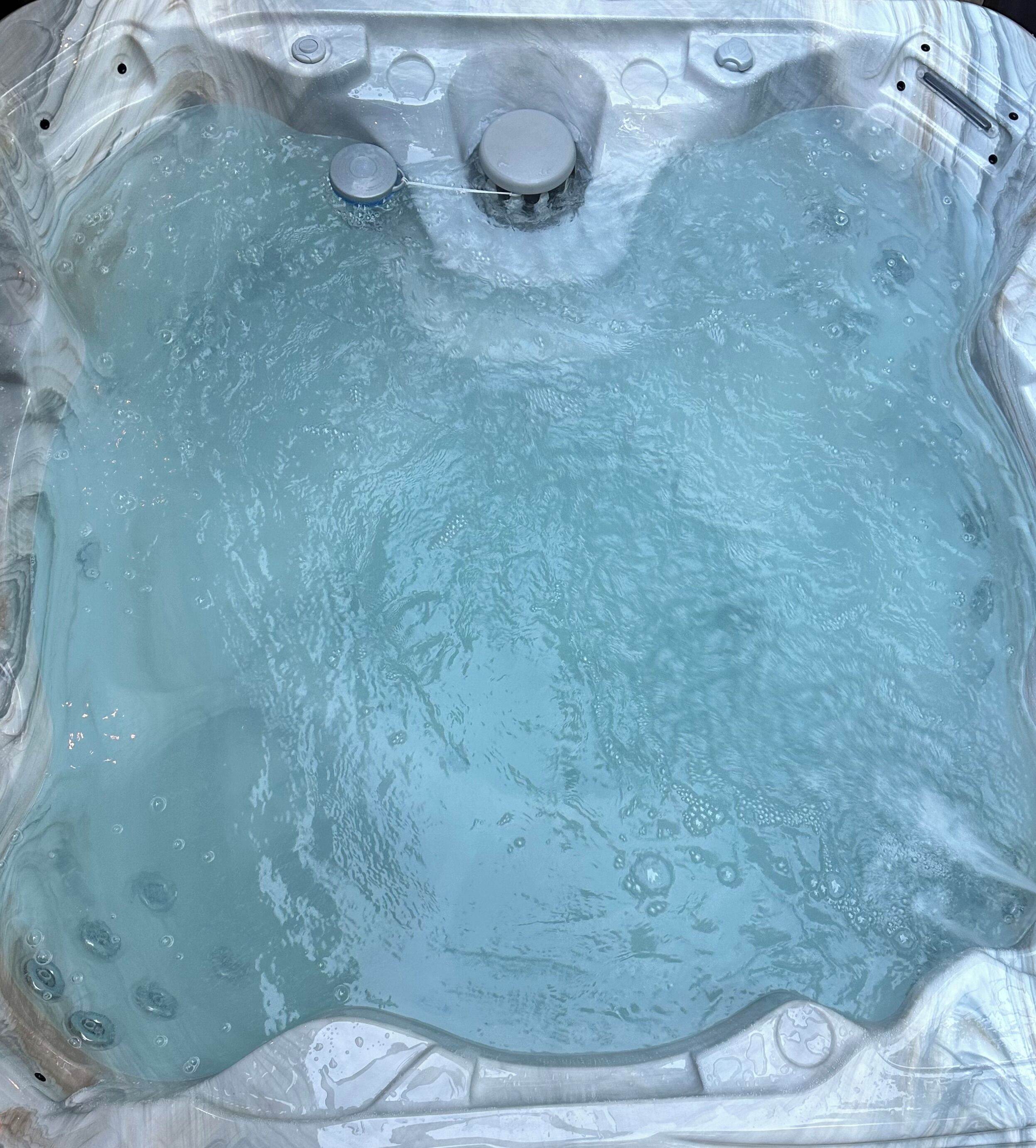 Una vasca idromassaggio con superficie d'acqua limpida, bolle visibili e un pannello di controllo con pulsanti e una manopola.