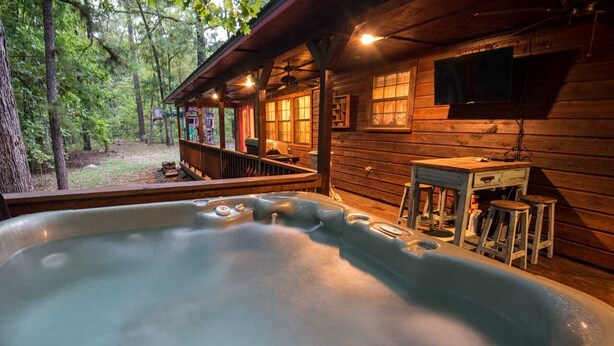 Uma banheira de hidromassagem em uma cabana de madeira com varanda, uma mesa e uma TV fixada na parede.
