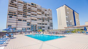 A hotel with a rooftop pool, multiple balconies, and a large building in the background. - Spacious Upgraded Oceanfront Gem, Great Views, Sleeps 6, Flexible Check-in Days (Ocean City)