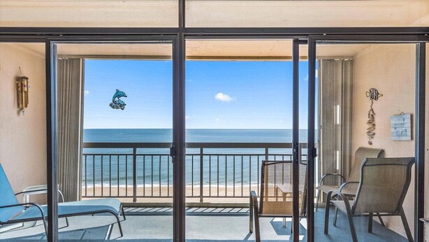 A balcony with a view of the ocean, a chair, a small table, and a decorative wall piece. - Spacious Upgraded Oceanfront Gem, Great Views, Sleeps 6, Flexible Check-in Days (Ocean City)