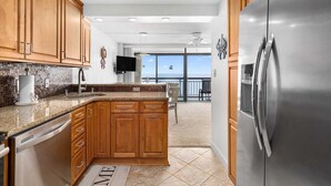 A modern kitchen with wooden cabinets, a stainless steel refrigerator, and a view to a balcony. - Spacious Upgraded Oceanfront Gem, Great Views, Sleeps 6, Flexible Check-in Days (Ocean City)