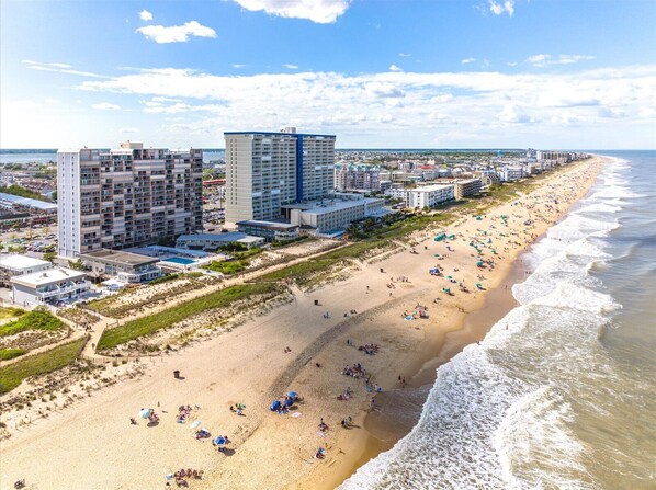 A coastal cityscape with a wide sandy beach, high-rise hotels, and a clear blue sky.
