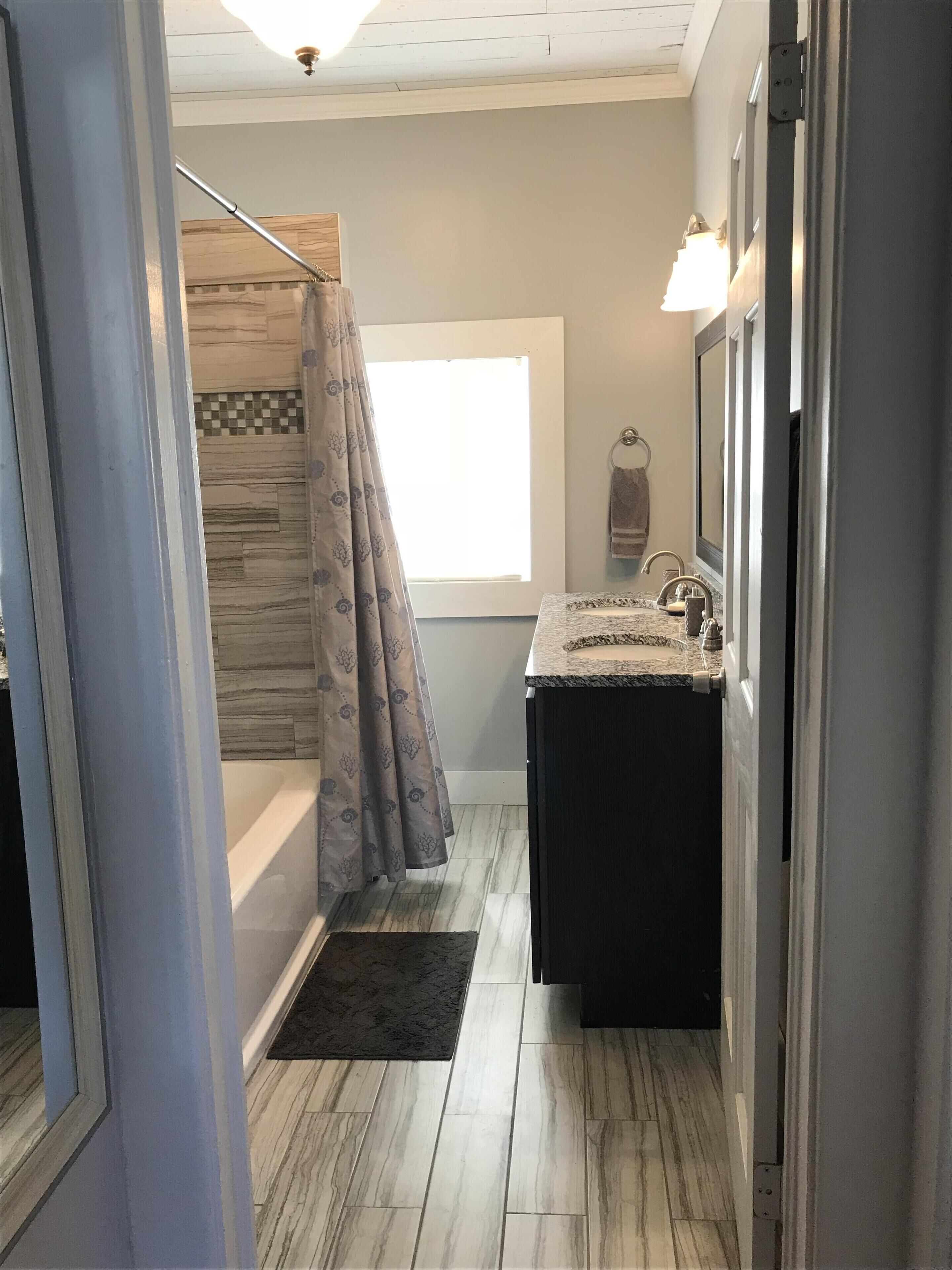 A bathroom with a bathtub, a shower with a curtain, a sink with a mirror, and a window.