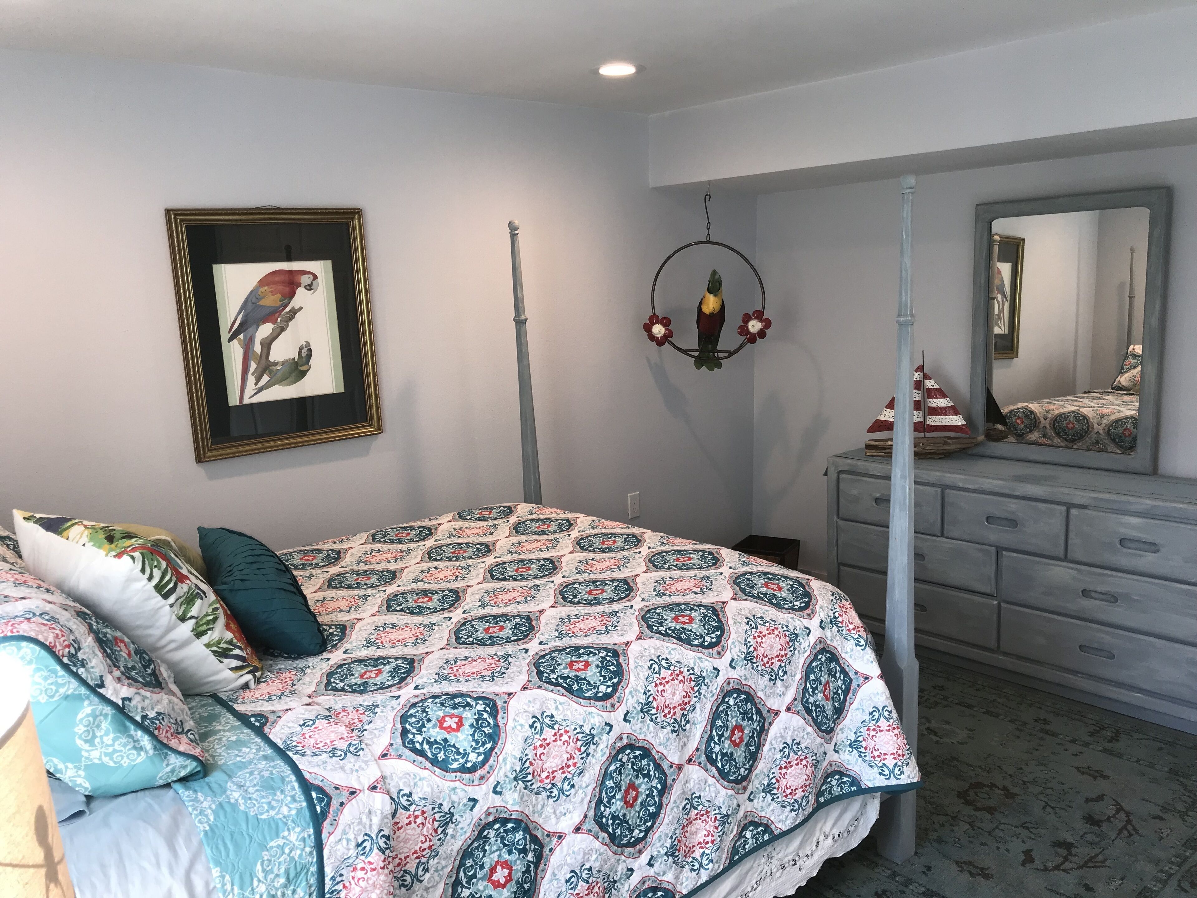Un dormitorio con cama con dosel, cómoda, espejo y un cuadro enmarcado de un pájaro.