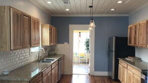 Una cocina con armarios de madera, encimeras de granito, un refrigerador de acero inoxidable y un comedor con una silla y una mesa.