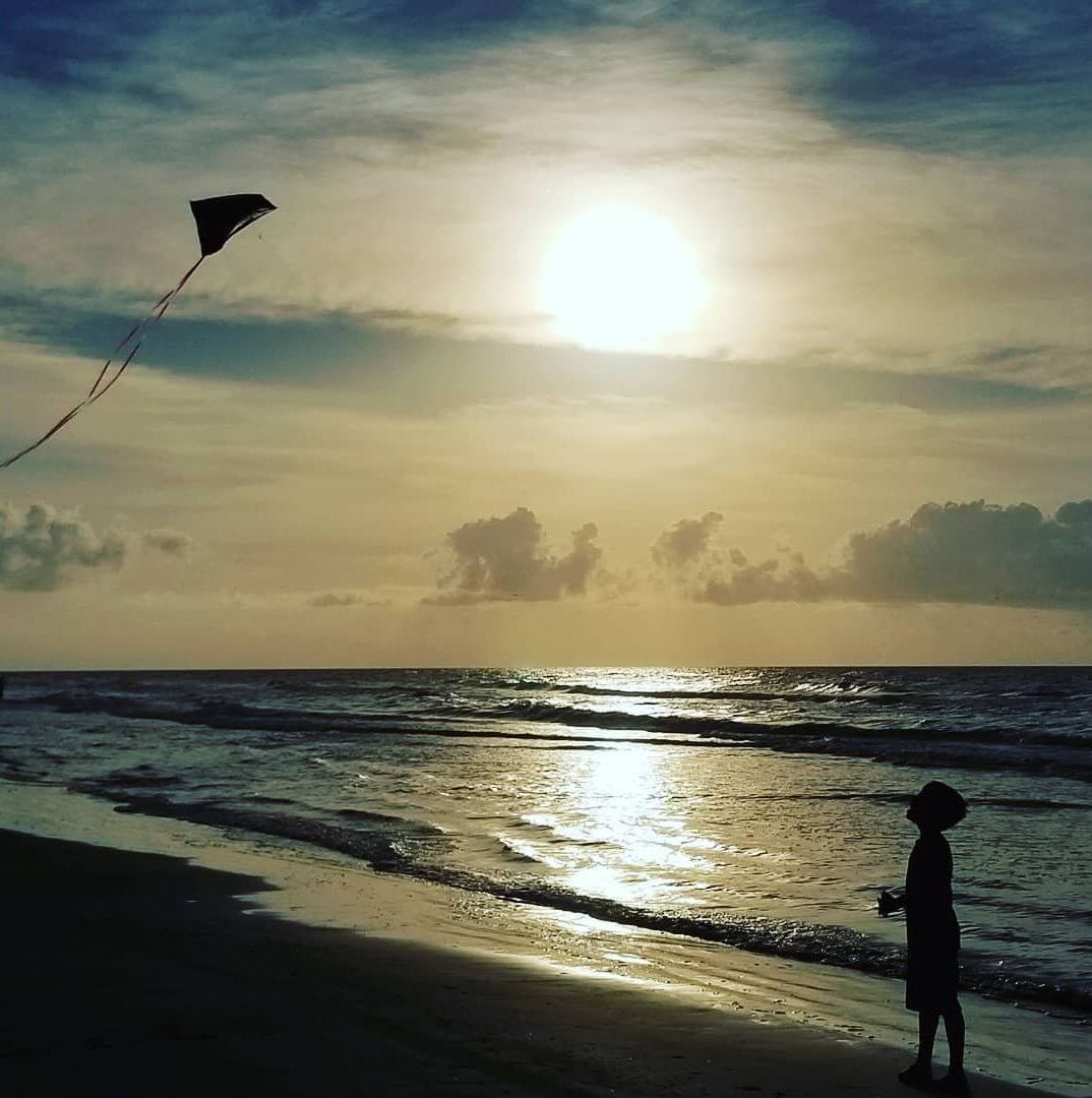 Escena de playa con una persona volando una cometa.