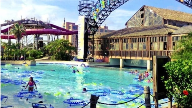 Una piscina con flotadores inflables, un tobogán acuático y un edificio de techo de paja.